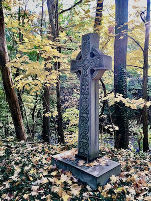 A grave marker in the shape of a cross, set amongst trees